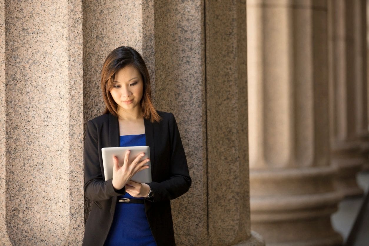 A woman standing in front of pillars holding an ipad.