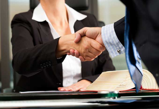 Two people shaking hands over a table.