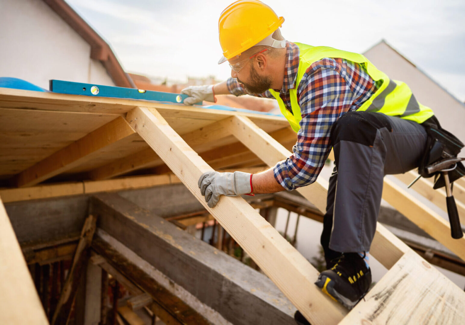 Mid-adult male Caucasian roofer, using level while working on a roof beam at the construction site